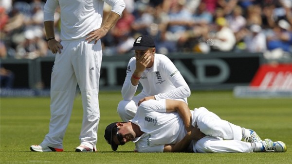 England's Joe Root (C) smiles as England's captain Alastair Cook lies hurt whilst fielding in the slips, after being hit the ball during play on the second day of the opening Ashes cricket test match between England and Australia at The Swalec Stadium in Cardiff, south Wales, on July 9, 2015. England were bowled out for 430. AFP PHOTO / IAN KINGTON RESTRICTED TO EDITORIAL USE. NO ASSOCIATION WITH DIRECT COMPETITOR OF SPONSOR, PARTNER, OR SUPPLIER OF THE ECB        (Photo credit should read IAN KINGTON/AFP/Getty Images)